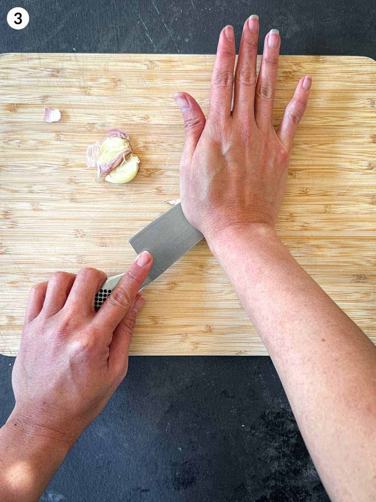 Smashing garlic cloves with a knife on a wooden chopping board