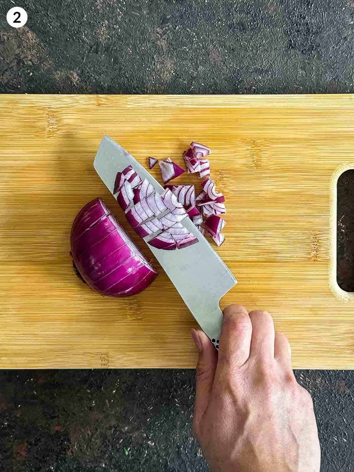 Dicing red onion on a wooden board with a knife