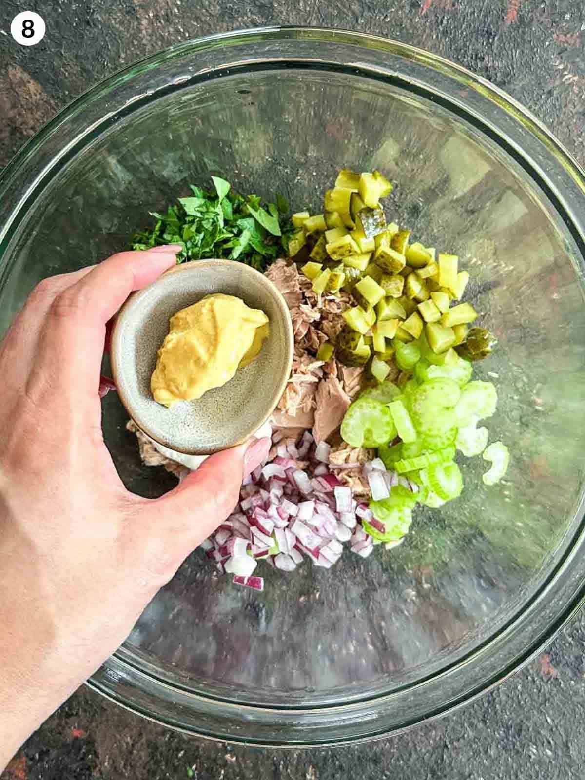 Adding mustard to a glass bowl of healthy tuna salad ingredients