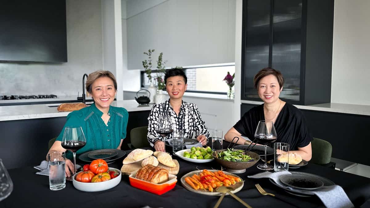3 women enjoying a dinner party with food and wine on a black dressed table