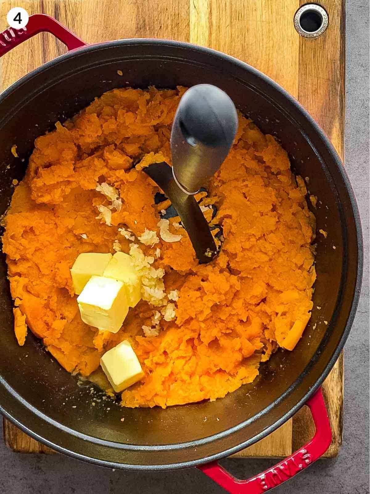 Adding cubes of butter into mashed sweet potatoes in a Ducth oven
