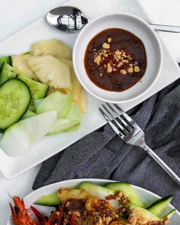 Salty Tamarind Dressing in a small white bowl served on a plate next to cut pineapple and cucumber