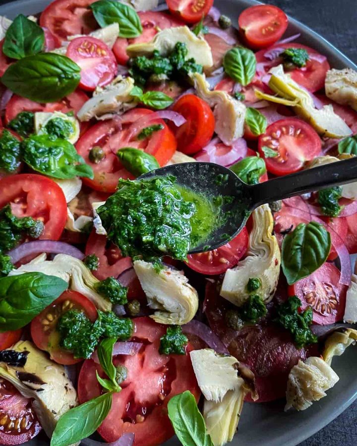 Adding a teaspoons of Basil and Mint Dressing onto tomato and artichoke salad