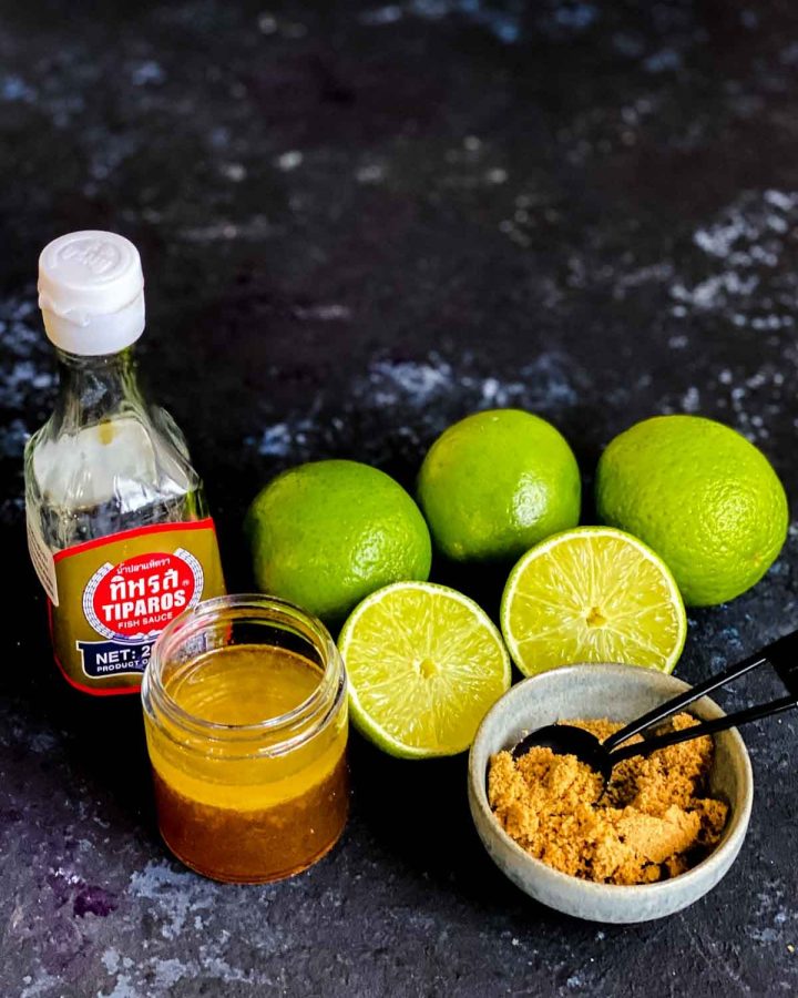 Fish Sauce Lime Vinaigrette in a jar with fresh limes, fish sauce bottle and brown sugar on the side