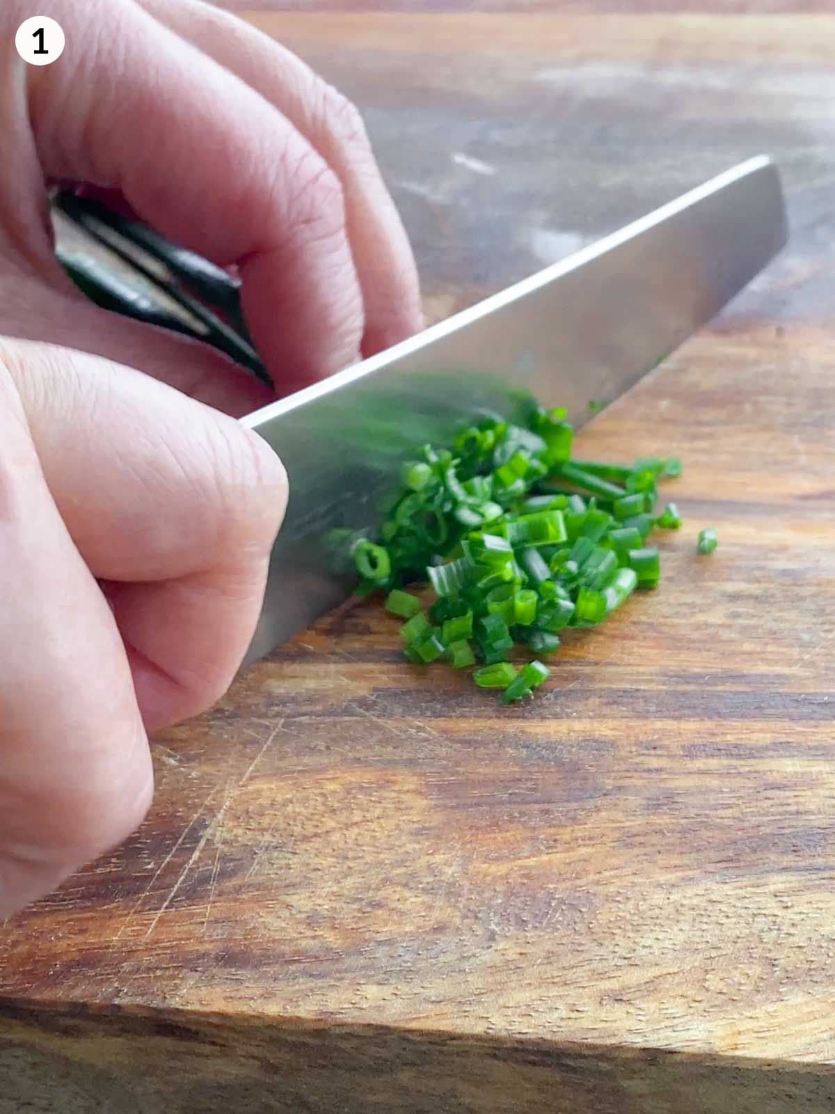 Knife chopping chives on a wooden board