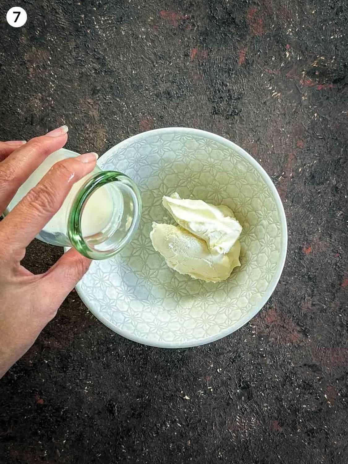 Adding milk from a glass jar to quark cheese in a small white bowl