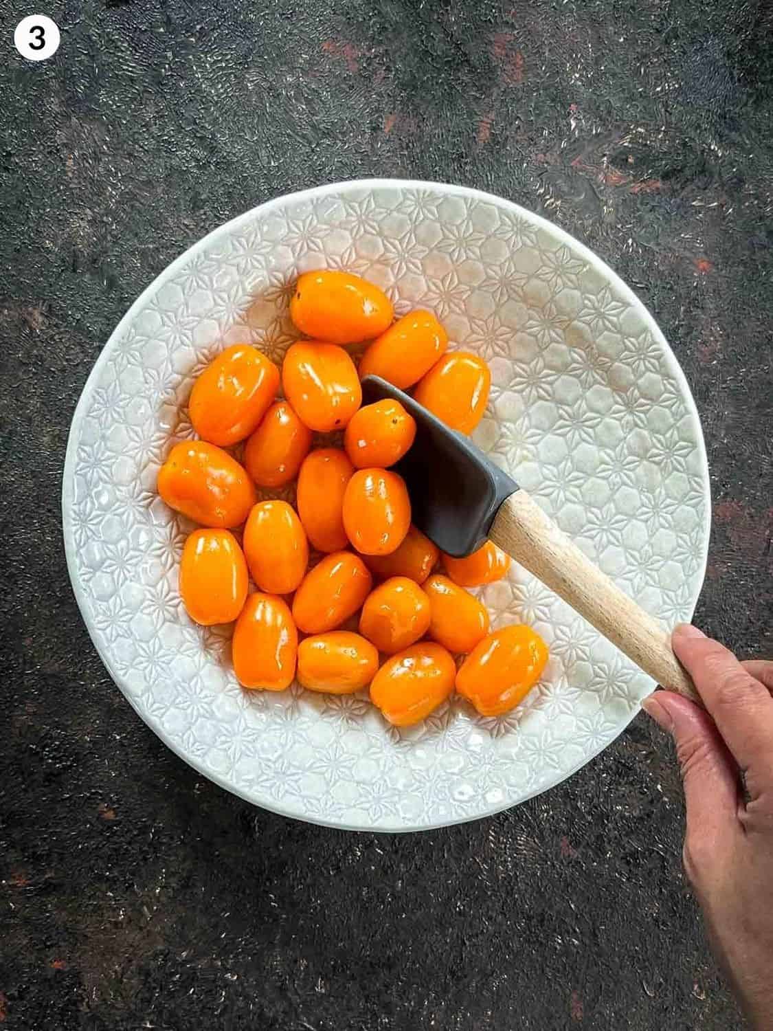 Mixing orange grape tomatoes in a white bowl