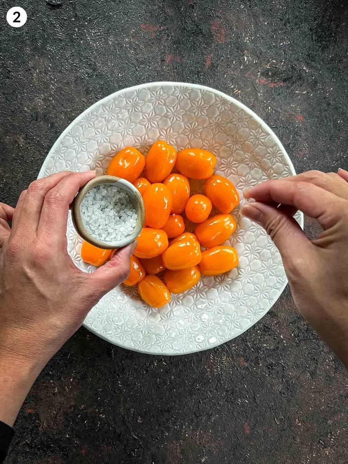 Adding salt over orange grape tomatoes in a white bowl