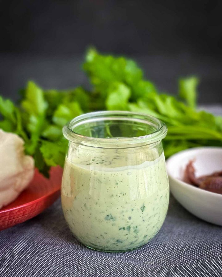 Lemon Parsley Anchovy and Garlic Dressing in a jar with garlic, anchovies and herbs in the background