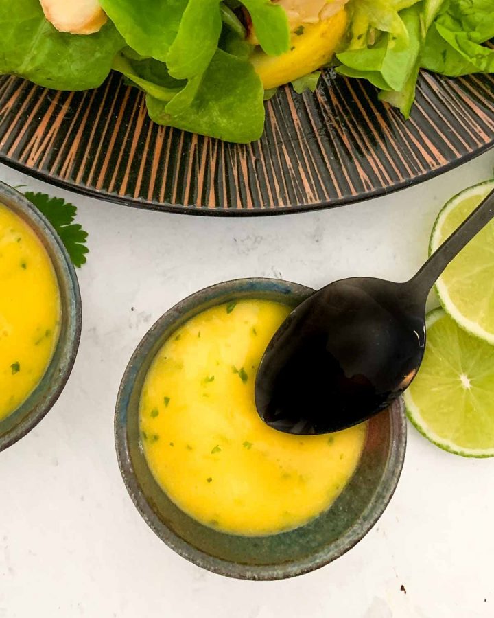 black teaspoon in a small bowl of Mango and Lime Dressing with limes on the side