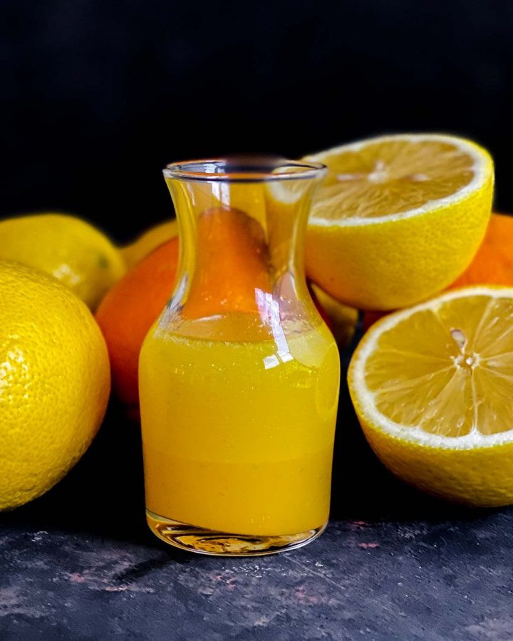 Orange Juice Dressing in a jar surrounded by half oranges and whole oranges