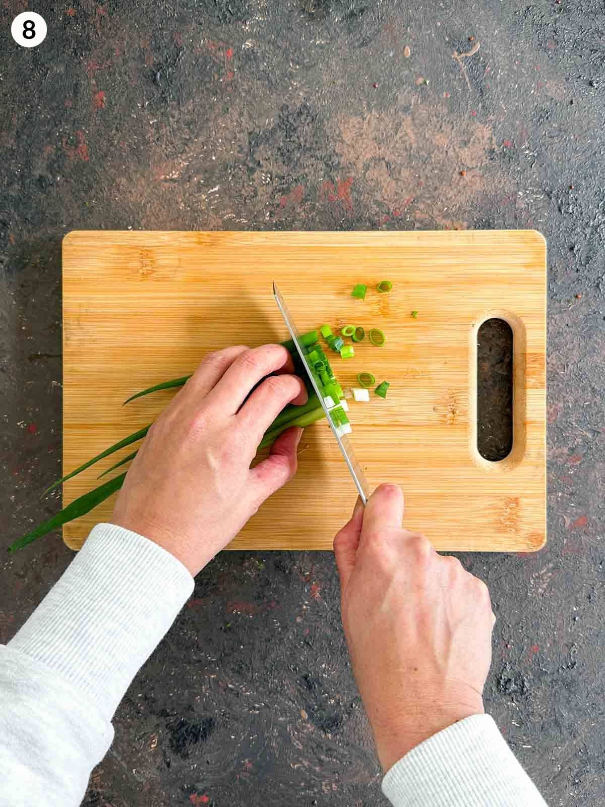 Chopping scallions with a knife on a wooden chopping board