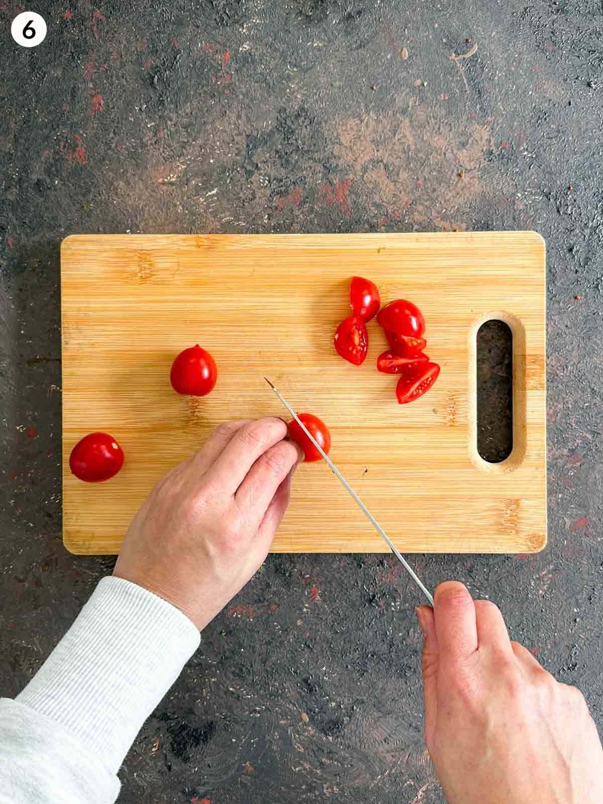 Chopping cherry tomatoes with a knife on a wooden chopping board