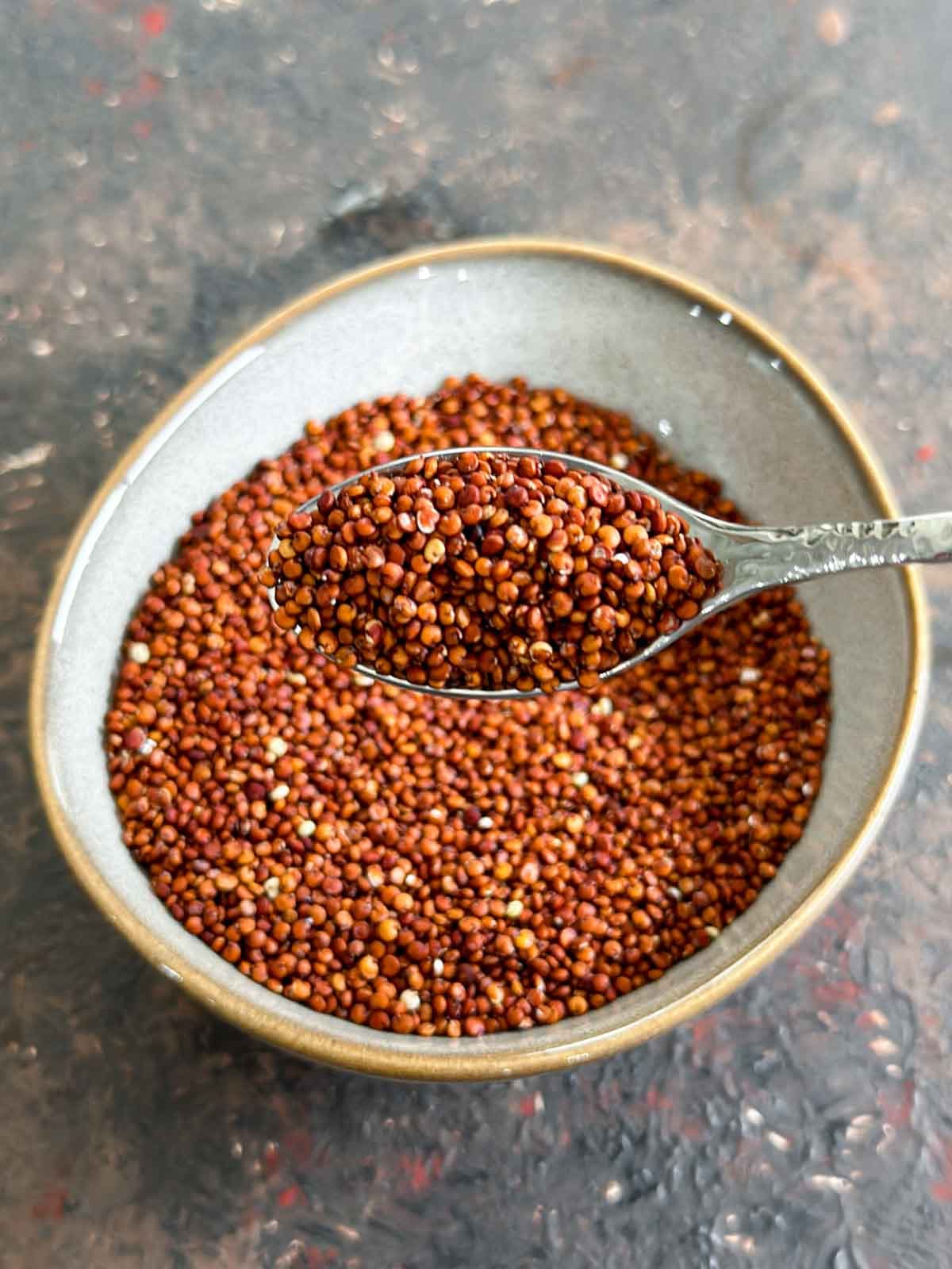 A teaspoon of uncooked red quinoa over a bowl of quinoa
