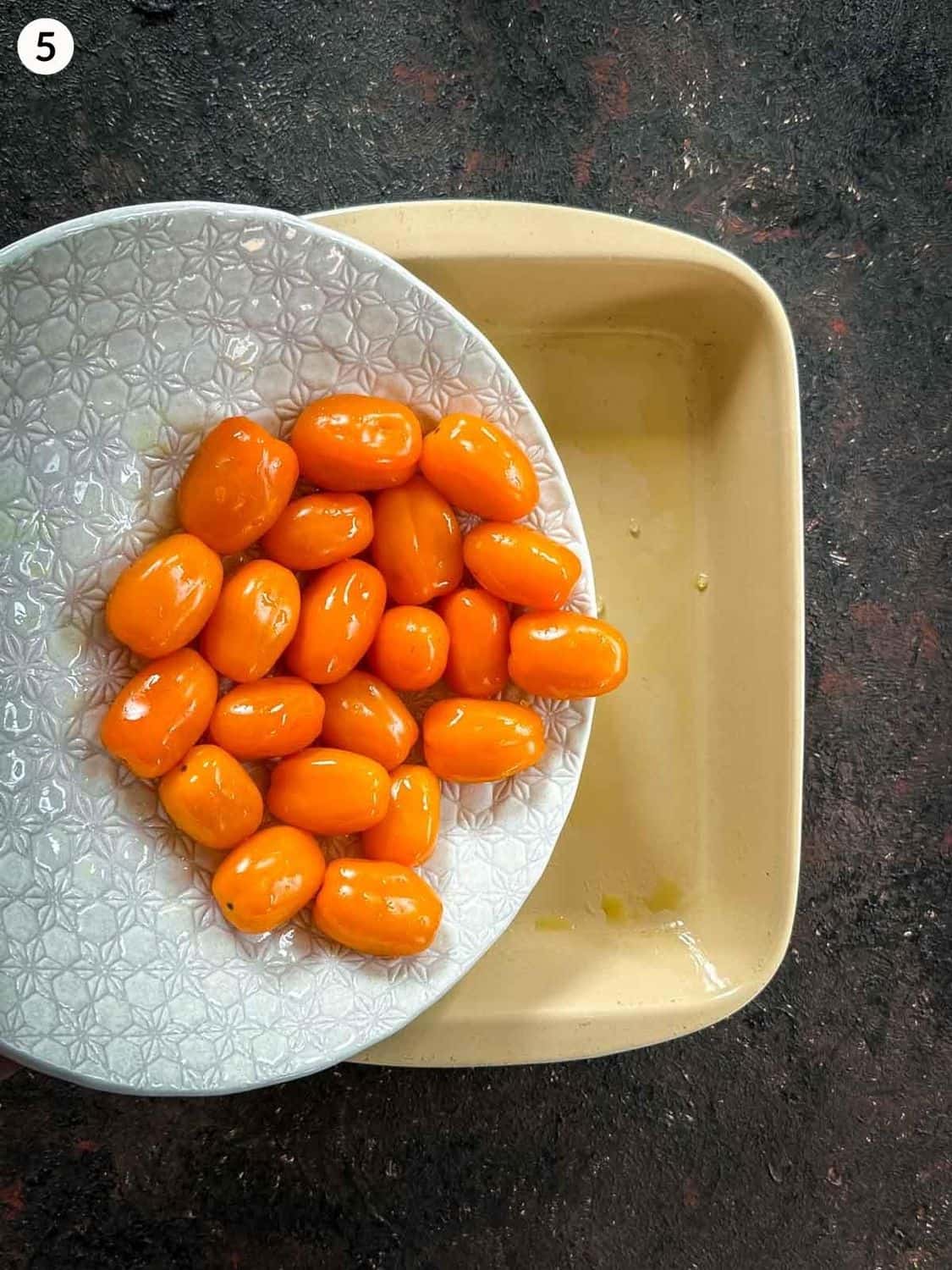 Adding orange grape tomatoes from a white bowl to an oiled baking dish