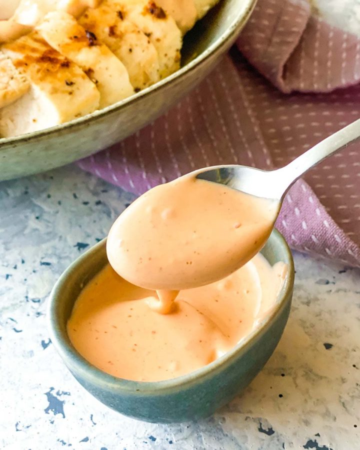 A teaspoon of Sriracha Aioli from a small blue bowl with salad on the side