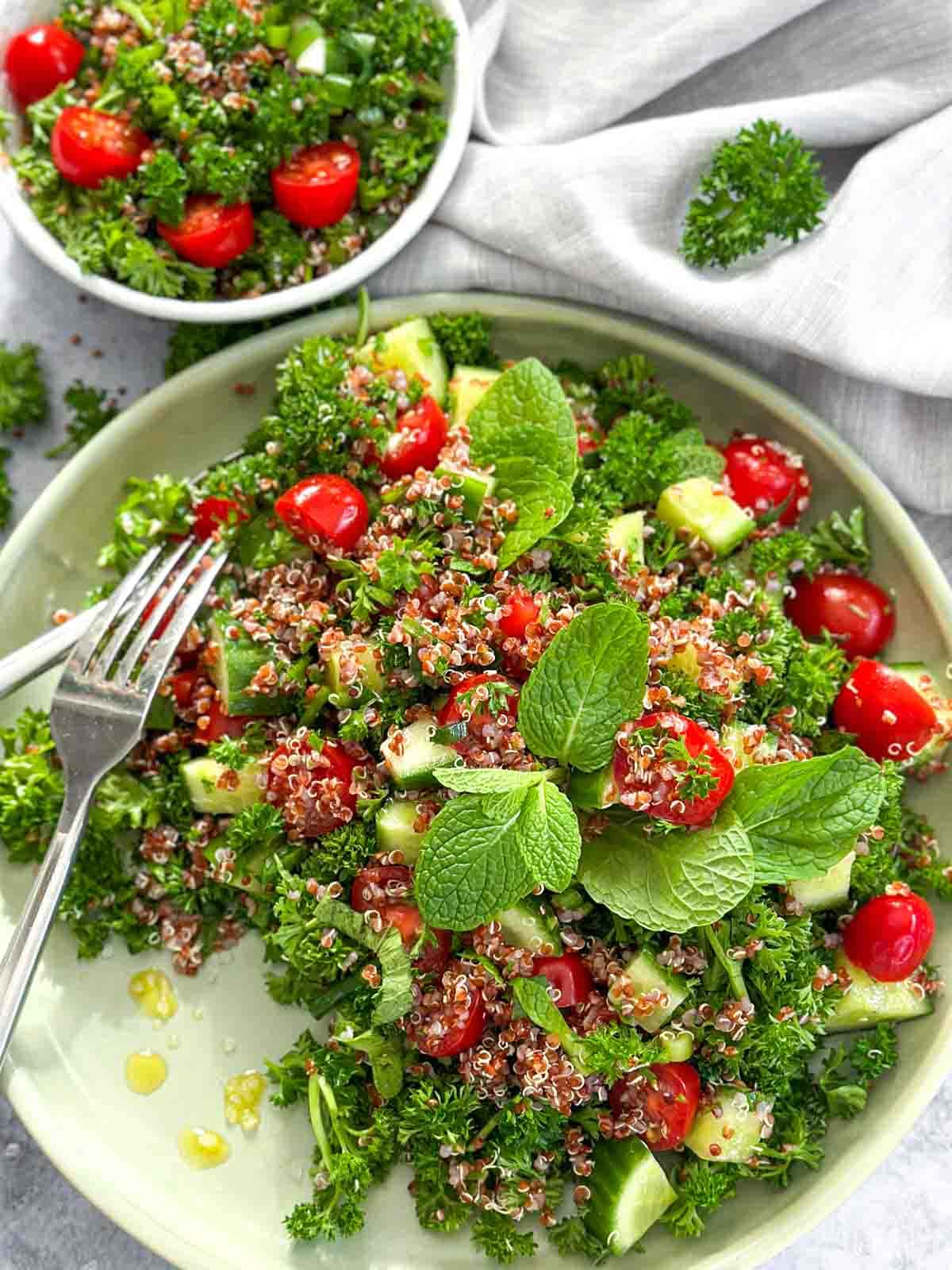 Vegan Quinoa Salad on a green plate with a fork and also a small bowl of the same salad with grey linen