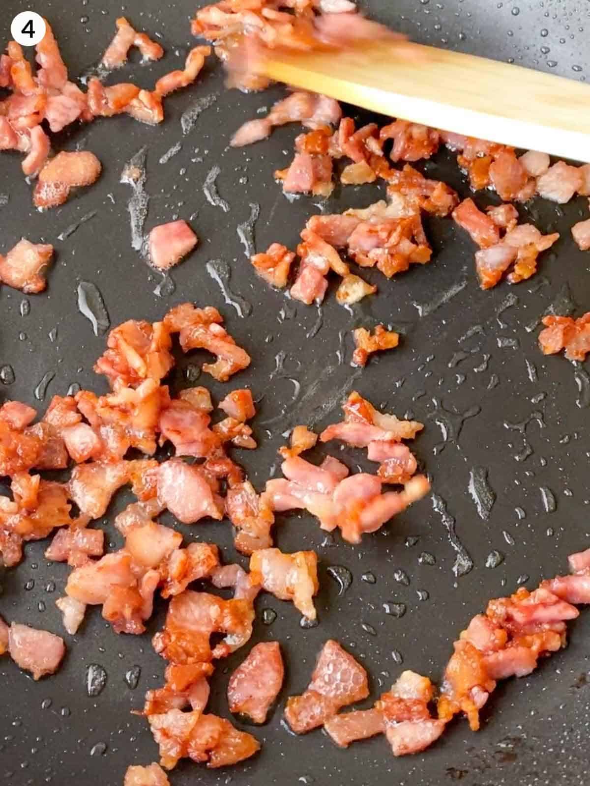 Frying bacon bits in a saucepan with a wooden spoon