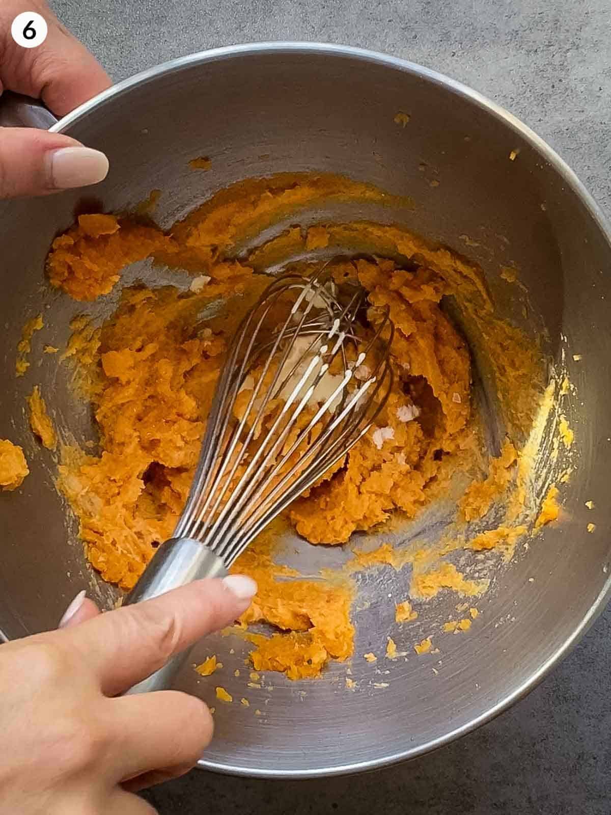 Whipping sweet potato mash with a whisk in a stainless steel mixing bowl