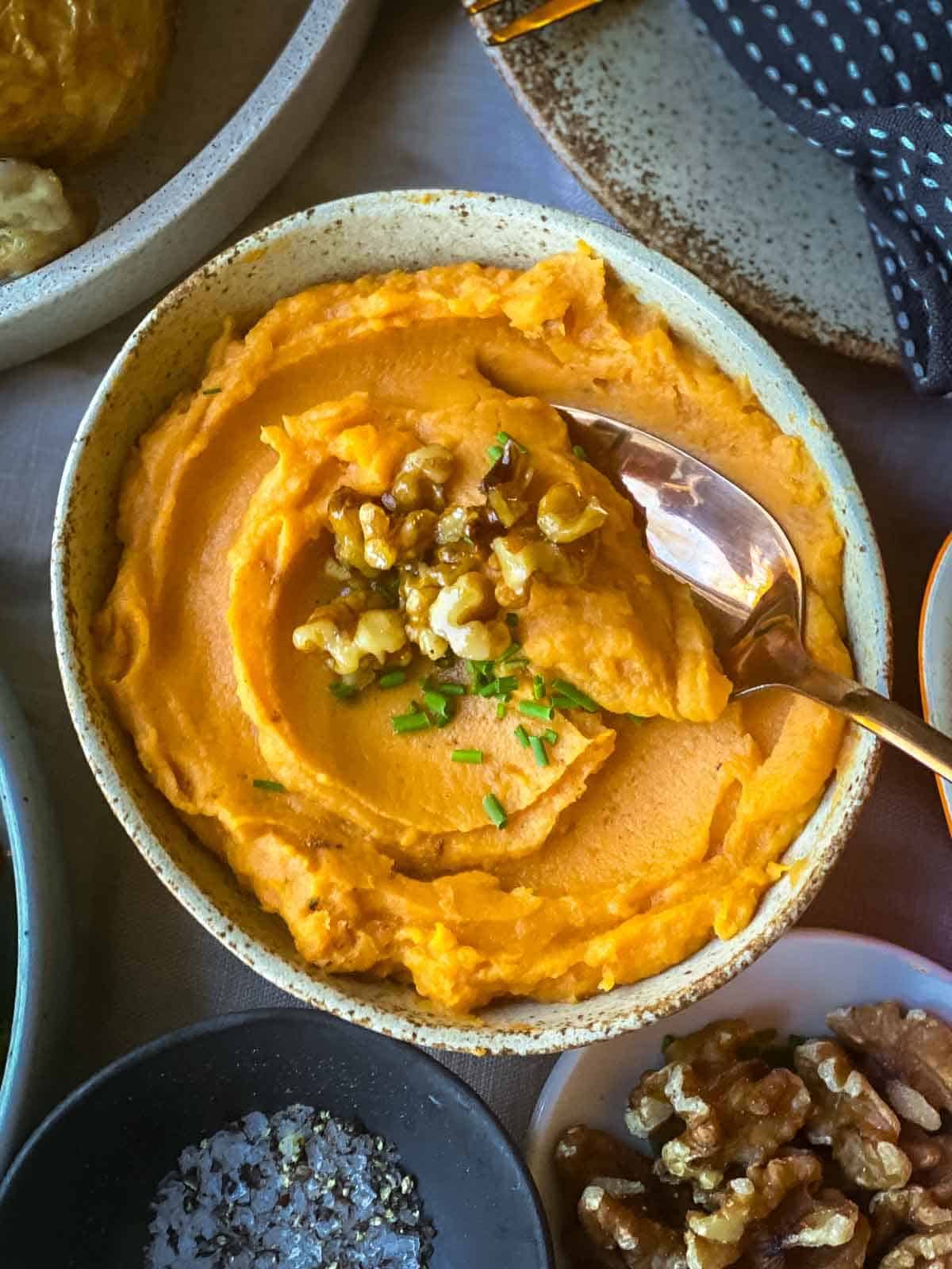 A spoon in a bow of whipped sweet potato next to a bowl of walnuts