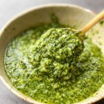 Gold spoon lifting a serve of basil mint pesto from a bowl