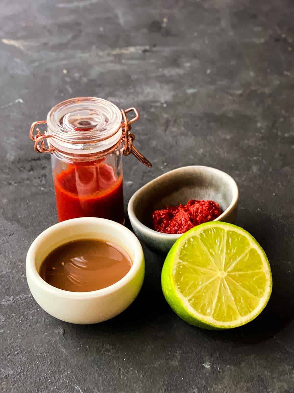 Jar of chilli tamarind dressing recipe with half a lime on the side, a bowl of tamarind and chilli paste.