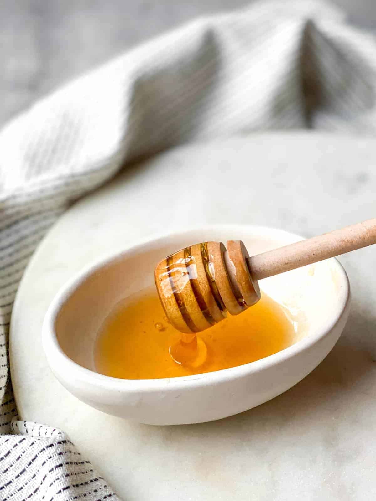 Honey dipper of honey from honey in a white bowl