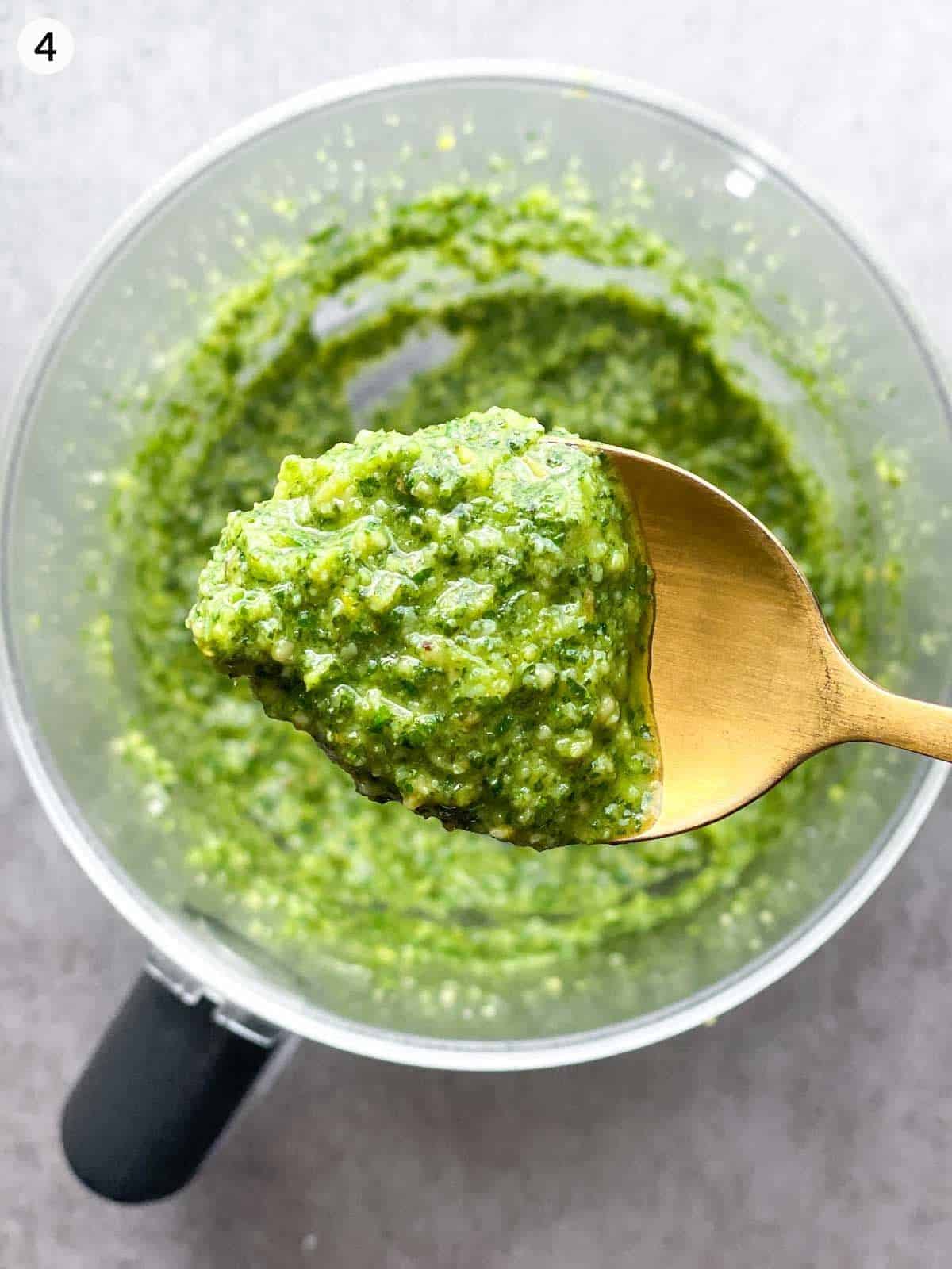 A gold spoon lifting basil mint pesto from a food processor