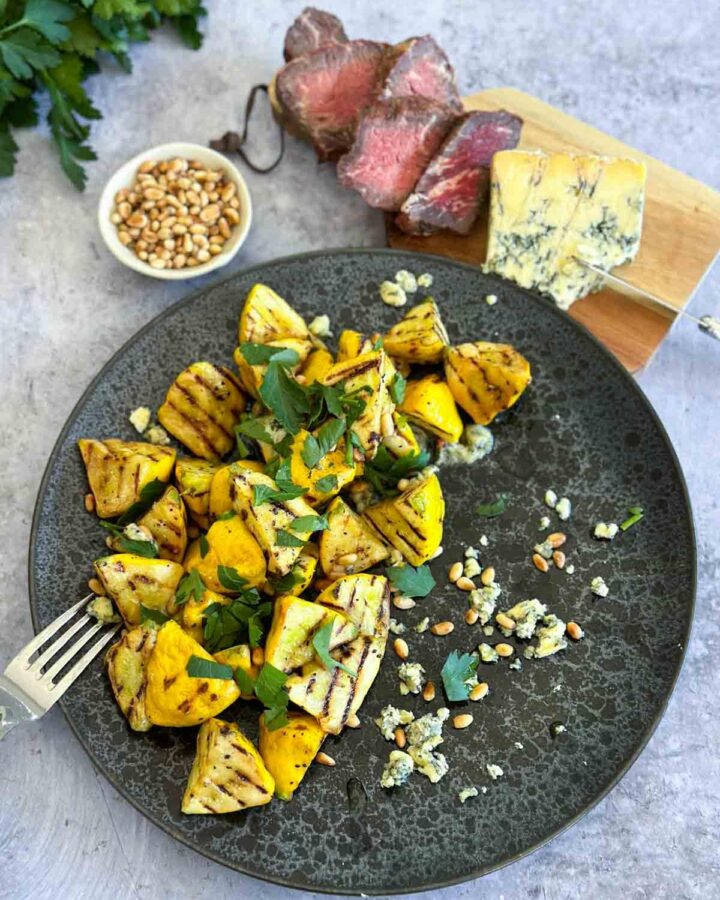 Grilled Pattypan Squash with Blue Cheese on a black plate served with rare steak and wedge of blue cheese on a wooden board