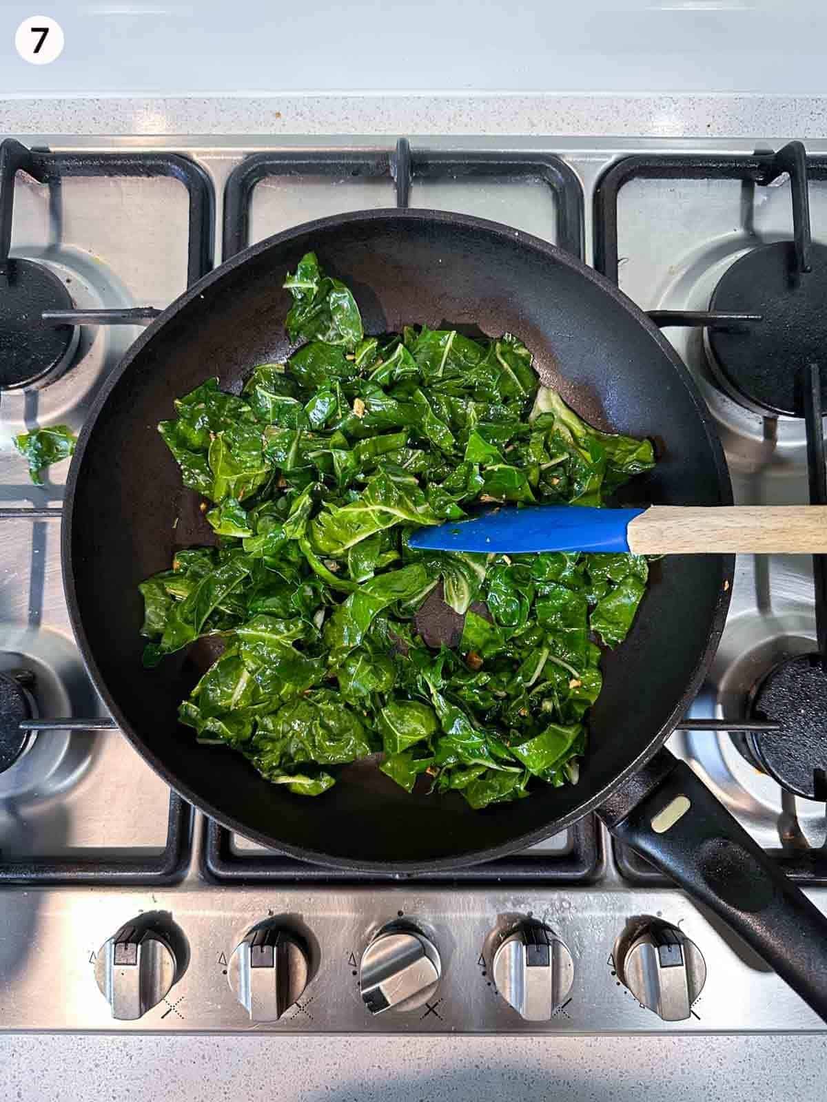 Sautéing silverbeet in a fry pan on a cooktop