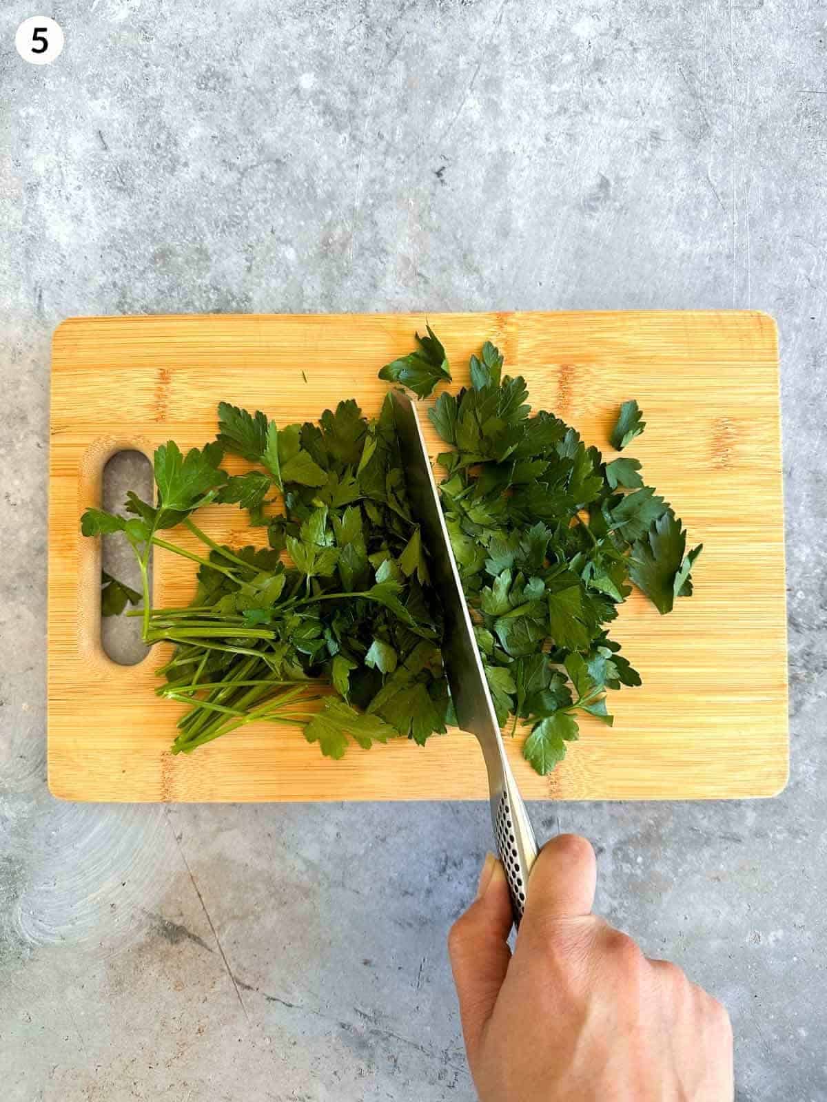 Cutting flat leaf parsley with a knife on a wooden board