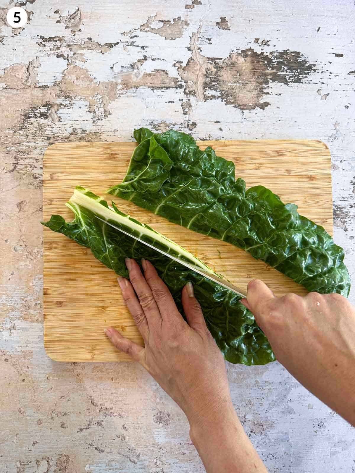 Removing the rib of the silverbeet with a knife on a wooden chopping board