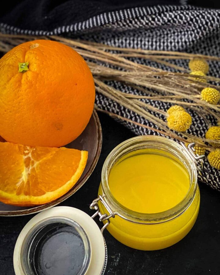 Orange salad dressing in a clear jar next to a bowl of oranges and blue napkins with yellow dried flowers