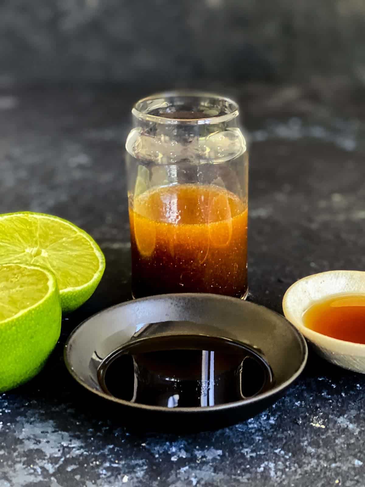 Tamari Lime Dressing in a jar next to 2 lime halves, bowl of tamari and bowl of organic rice malt syrup